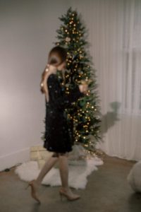 Pretty young woman dressed in sparkly dress in front of a Christmas tree