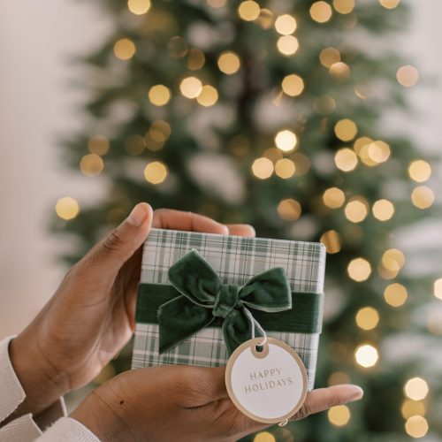 hands holding a beautifully wrapped gift in front of a christmas tree