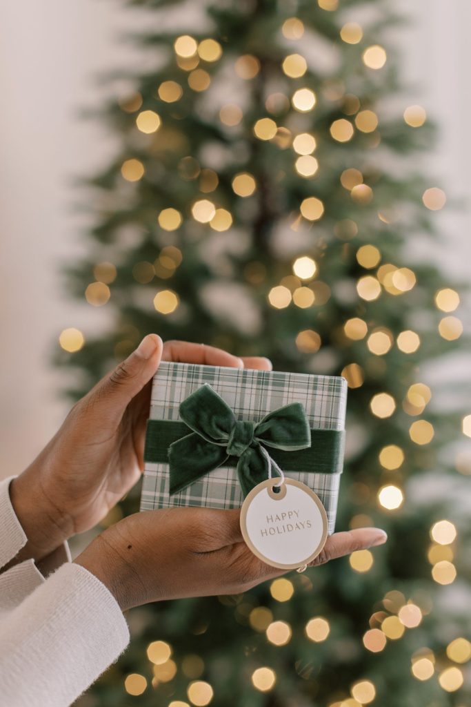 hands holding a beautifully wrapped gift in front of a christmas tree