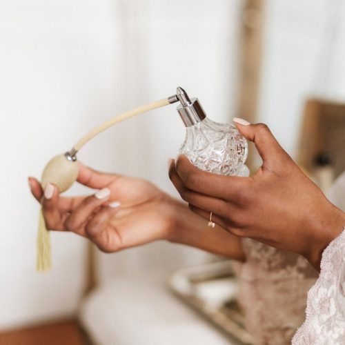 Woman with beautiful hands spraying perfume on chest