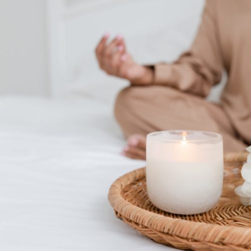 Woman sat on bed meditating with a lit white candle