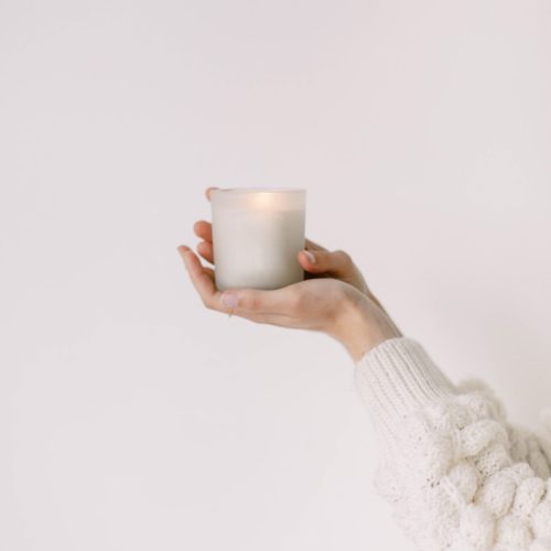 Woman's arms and hands in white sweater holding a white candle